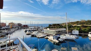 Un puerto deportivo con varias embarcaciones amarradas, un edificio de techo plano y un cielo despejado con algunas nubes.