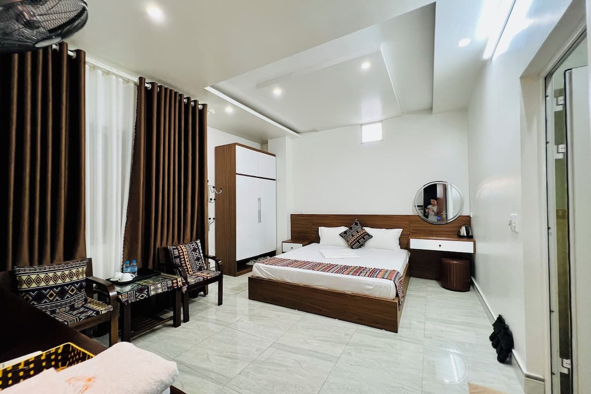 A modern hotel room with a bed, bedside table, chair, wardrobe, and a large mirror.