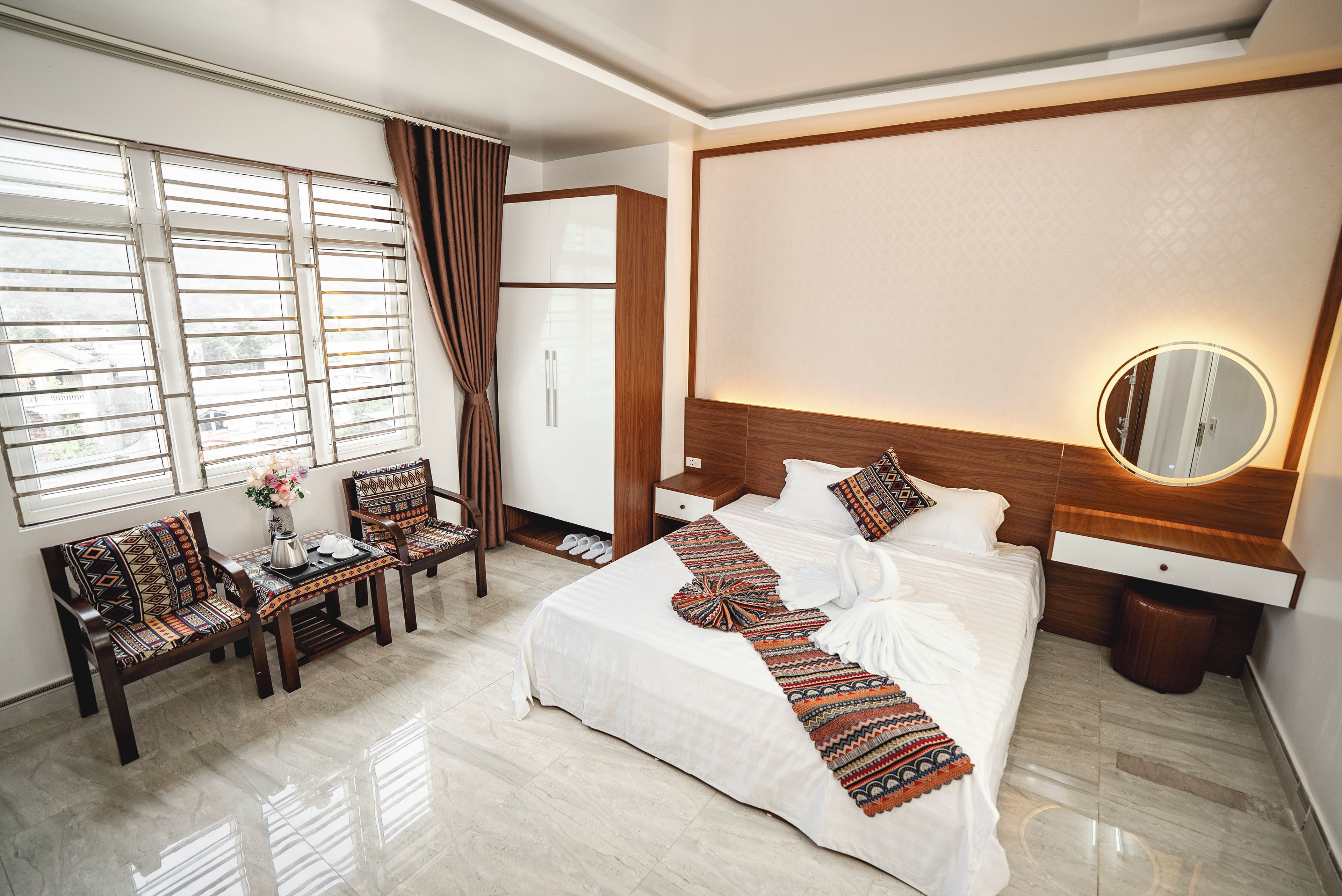A hotel room with a bed, a desk, a chair, a mirror, and a window with curtains.
