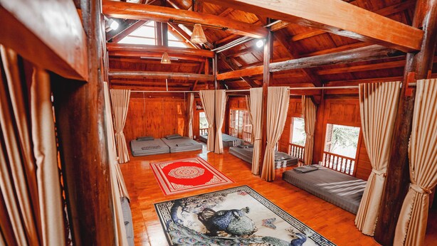 Ein Holzblockhaus-Interieur mit einem großen Pfauen-Teppich, mehreren Betten und Vorhängen.