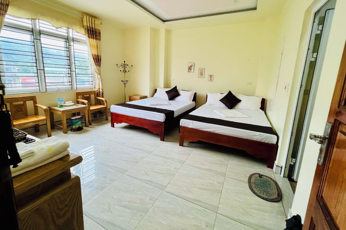 A hotel room with two beds, a desk, a chair, a coat rack, and a window with curtains.