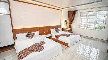 A hotel room with two beds, a wooden headboard, a bedside table with a mirror, and a window with curtains.