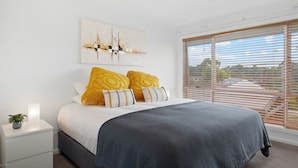 A bedroom with a bed, a nightstand, a potted plant, and a window with blinds. - House Allinga, great for large or multiple families. (Jindabyne)