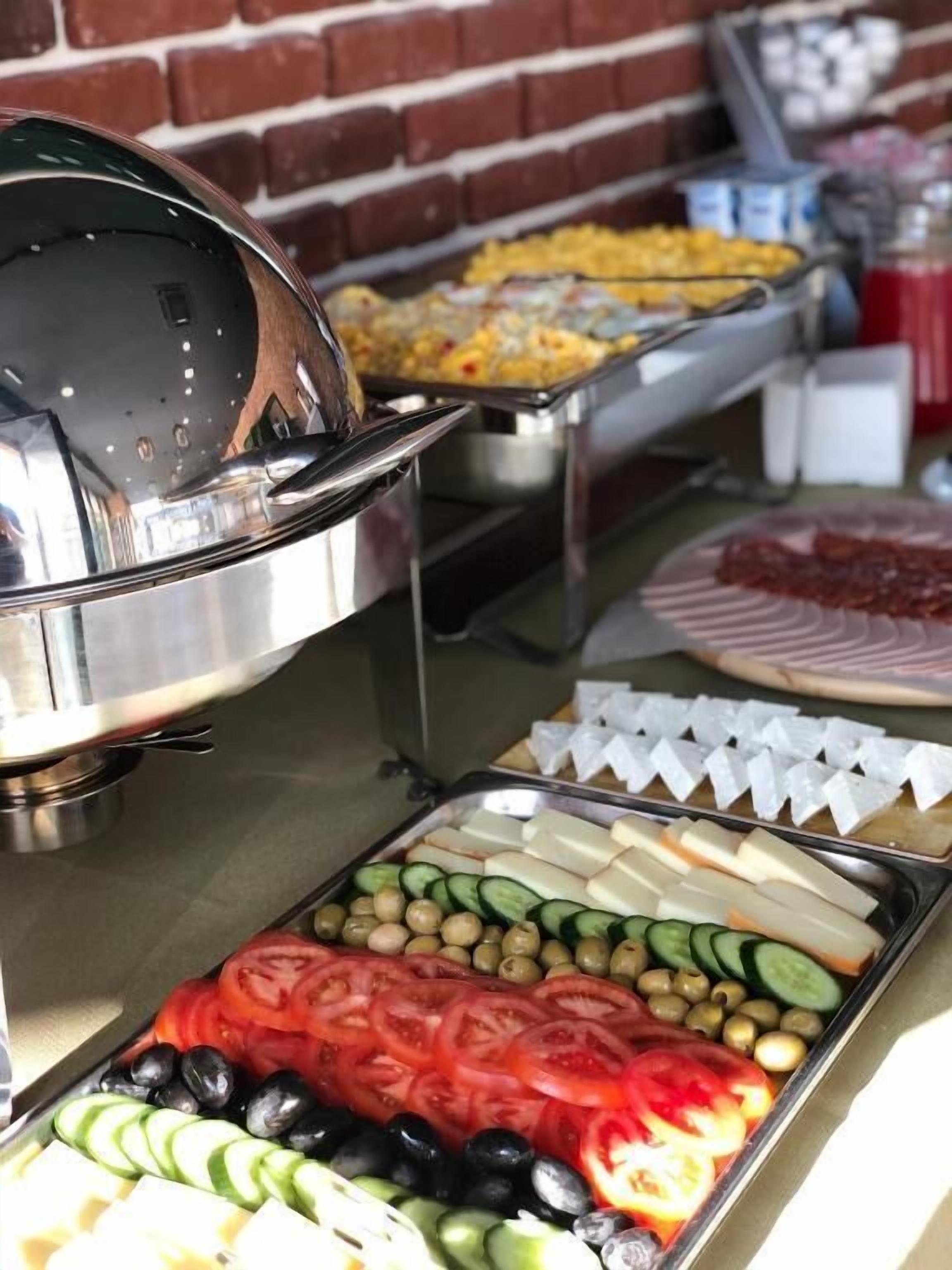 A buffet with various food items including sliced tomatoes, cucumbers, olives, and cheese.