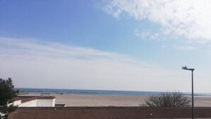 Vista de playa con cielo despejado, costa lejana y un farol.