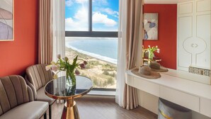 Ein Zimmer mit großem Fenster mit Blick auf einen Strand, einem runden Tisch mit Blumenvase und einer Couch.