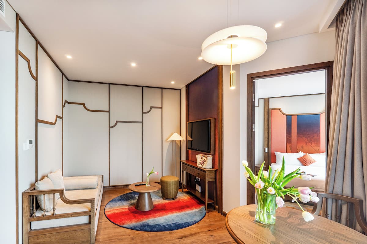 Habitación de hotel moderna con sofá, una mesita redonda, televisor, chimenea y vistas a la ciudad.
