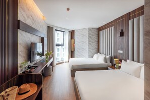 Habitación de hotel con dos camas, televisión, escritorio con computadora y ventana con vista a edificios.