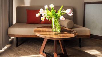 A modern living room with a round wooden table, a beige sofa with a red pillow, and a vase of white tulips.