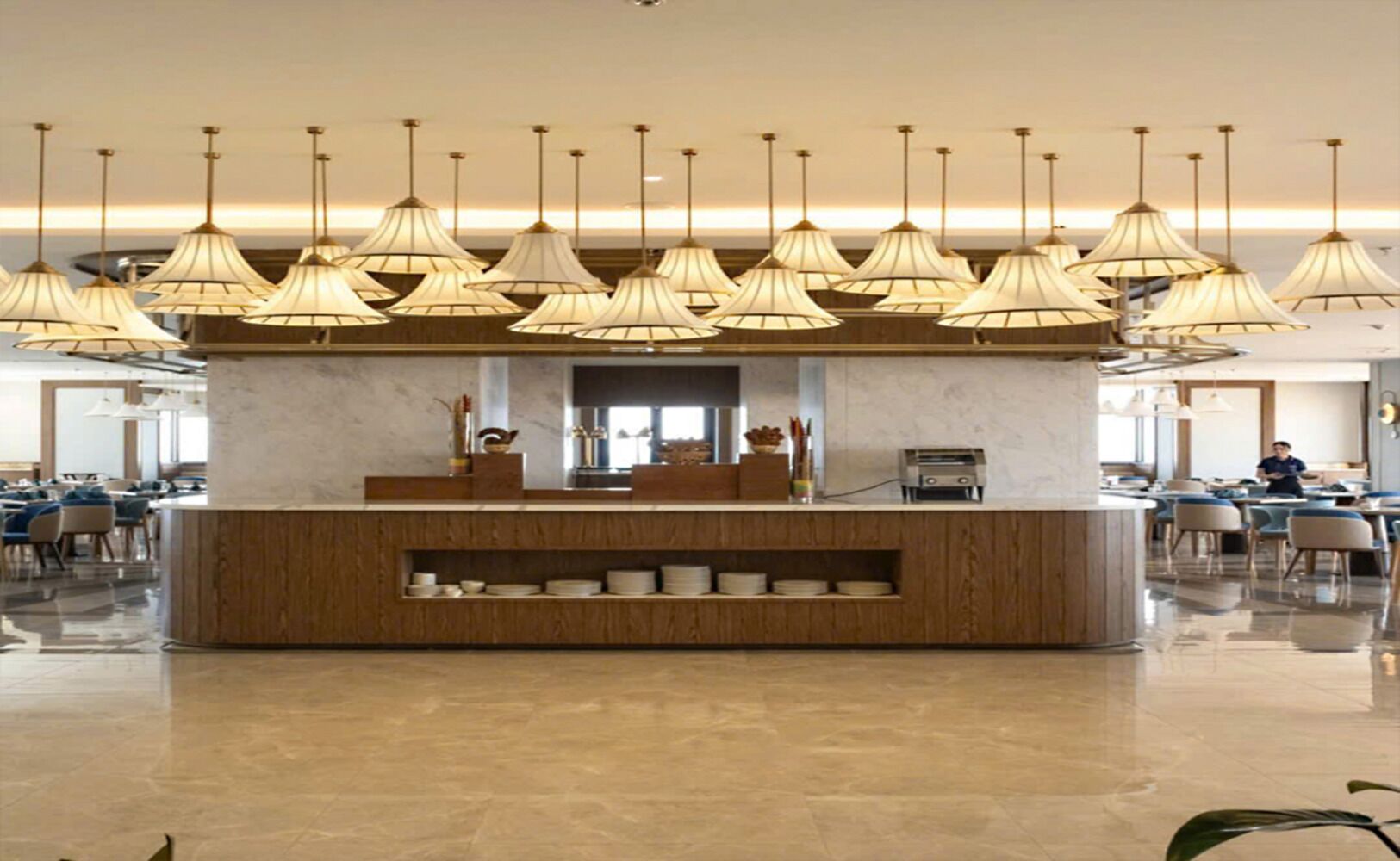 A modern hotel lobby with a central reception desk, multiple pendant lights, and a polished marble floor.
