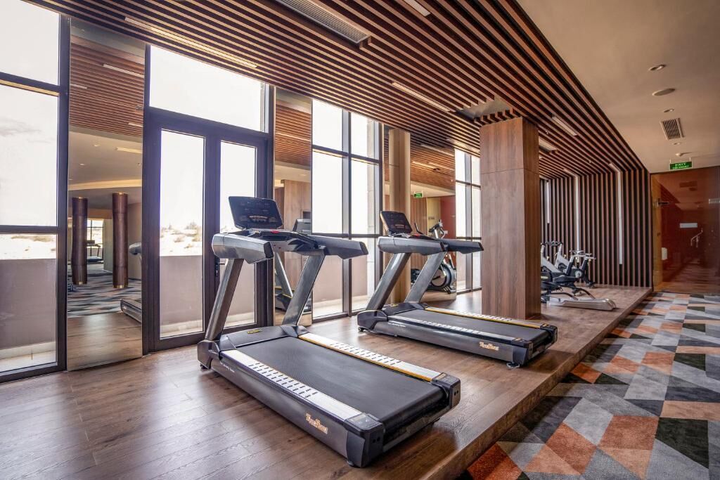 Ein Fitnessraum mit Laufbändern, Ergometer und einem gemusterten Teppich.
