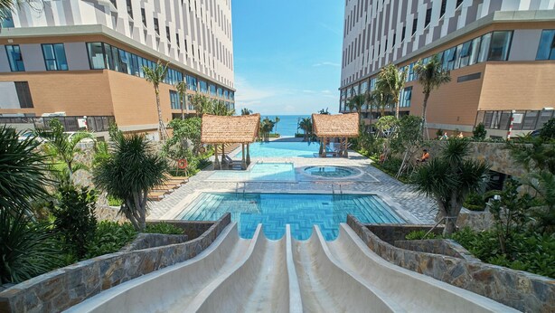 Ein Hotelpool mit Wasserrutsche, Palmen und Blick aufs Meer.