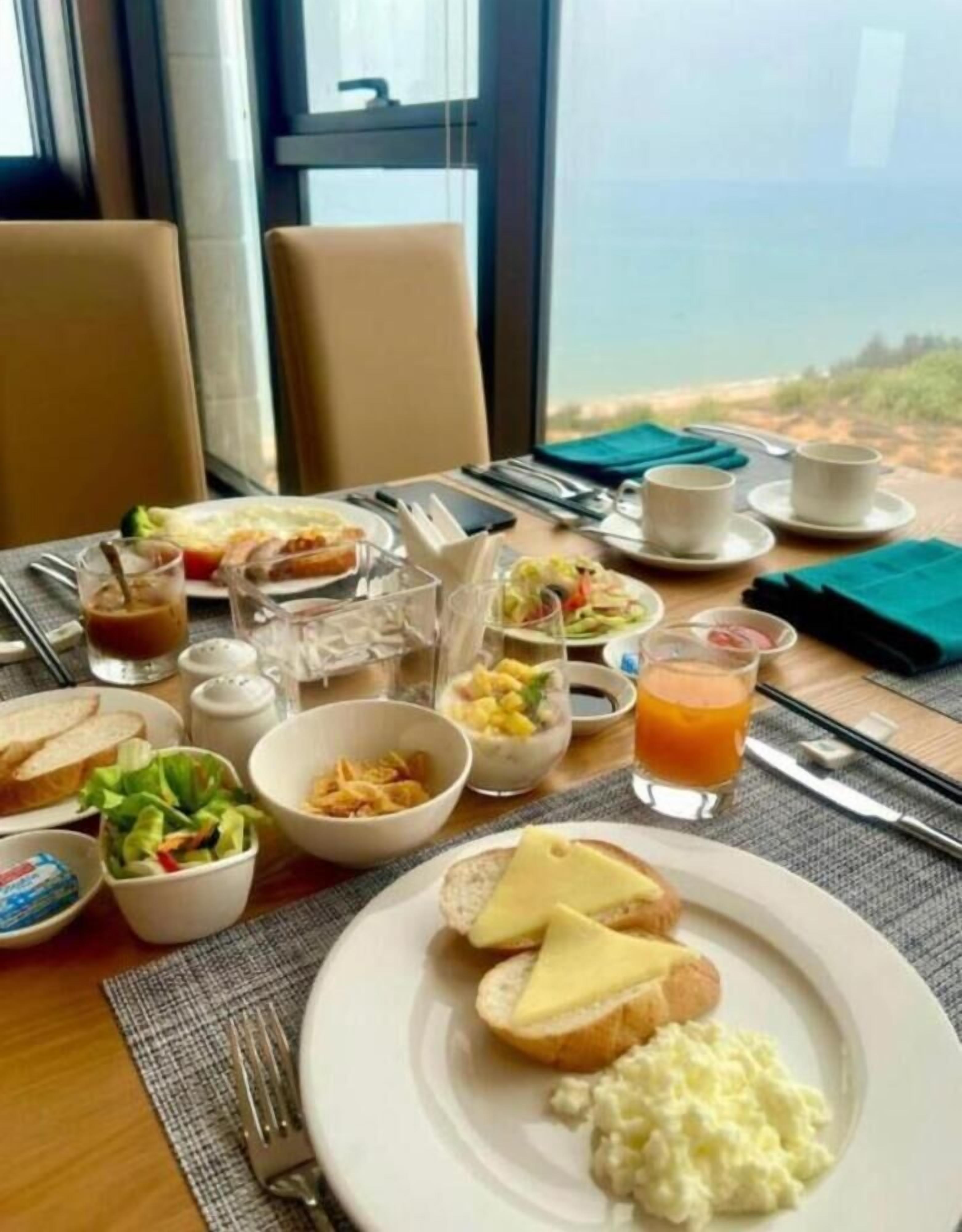 Une table de petit-déjeuner avec divers plats, notamment des toasts, des œufs brouillés et une salade, le tout disposé devant un paysage pittoresque.