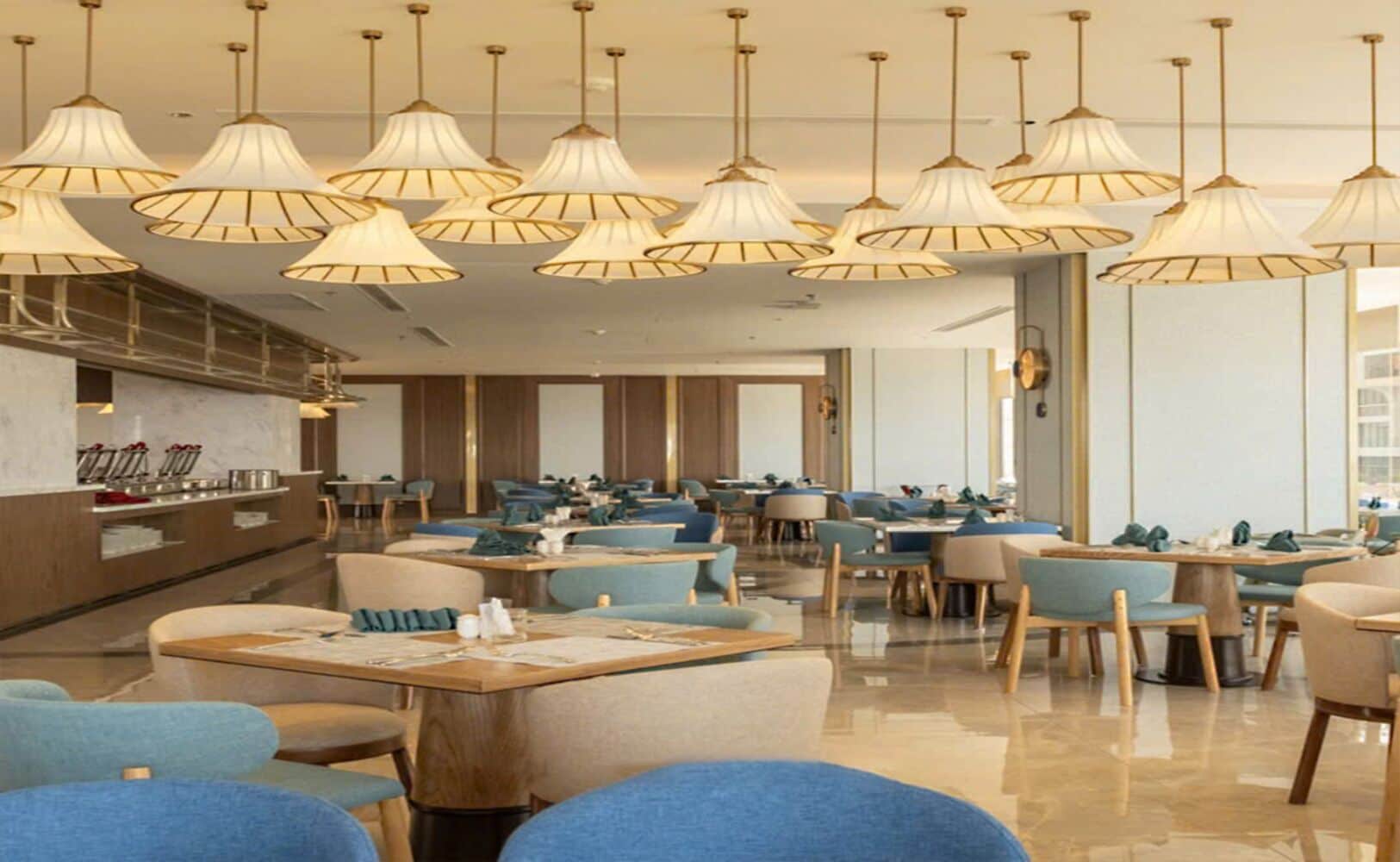 Un restaurant moderne doté de plusieurs tables et chaises, d’un bar et d’un éclairage suspendu.