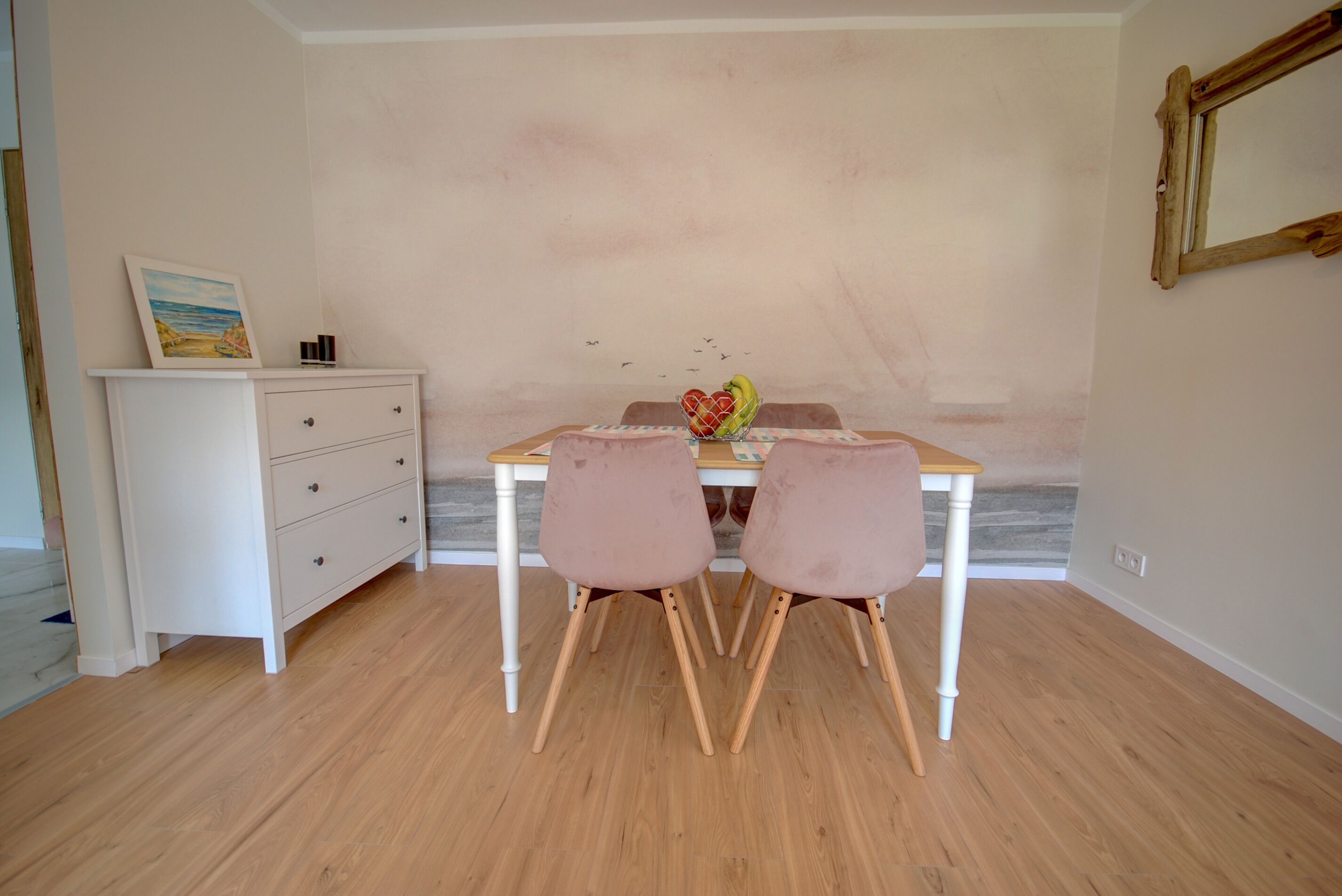 A dining area with a wooden table, two chairs, a white dresser, and a framed picture on the wall.