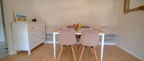 A dining area with a wooden table, two chairs, a white dresser, and a framed picture on the wall.