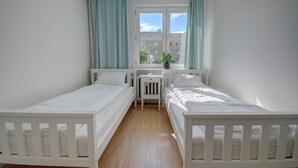 Un dormitorio con dos camas individuales, un escritorio pequeño, una silla y una ventana con cortinas.