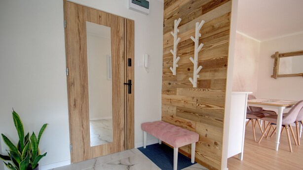 Un pasillo con puerta de madera, un banco, una planta en maceta y un comedor con sillas y una mesa.