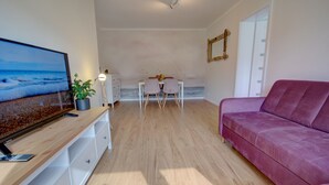 Una sala de estar moderna con televisor de pantalla plana, una mesa de centro de madera, un sofá rosa y un comedor con una mesa y sillas blancas.