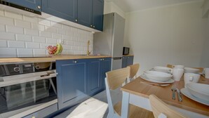 Una cocina moderna con armarios azules, un salpicadero de azulejos blancos, un refrigerador de acero inoxidable y una mesa de comedor de madera con sillas blancas.