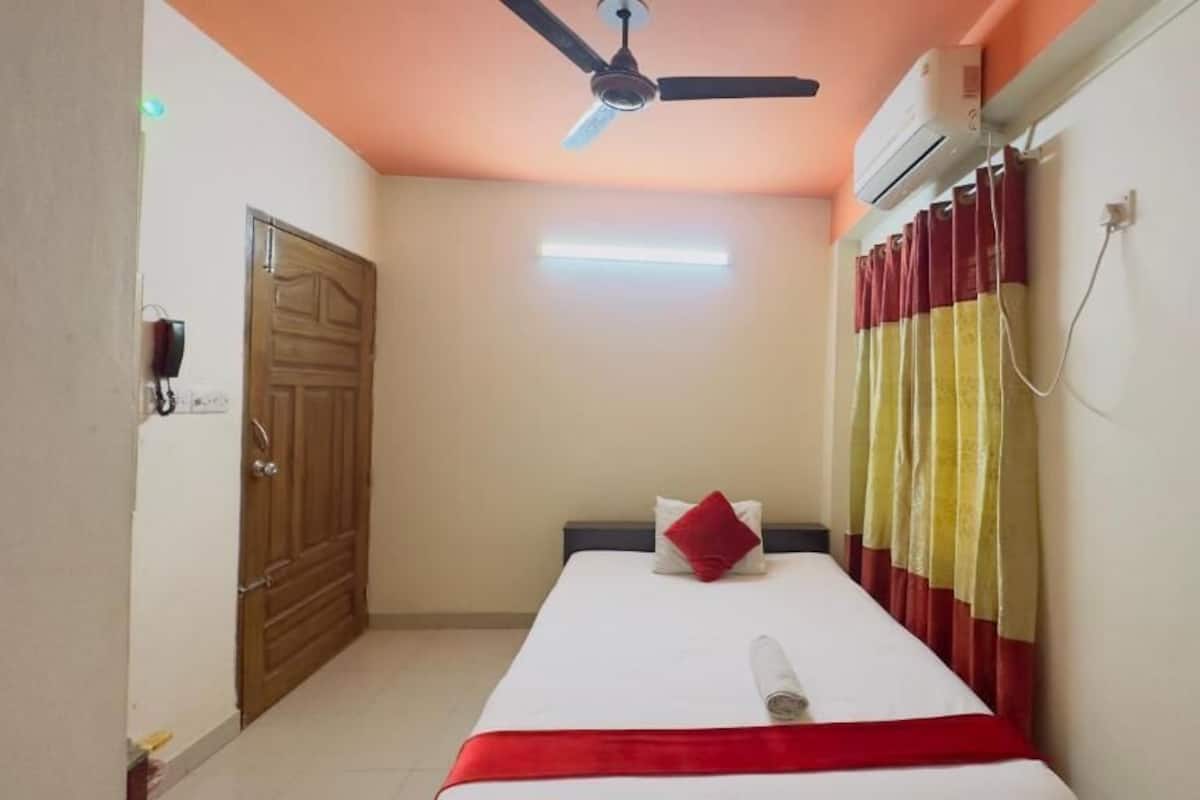 A hotel room with a bed, a ceiling fan, an air conditioning unit, a door, and a wall-mounted light.