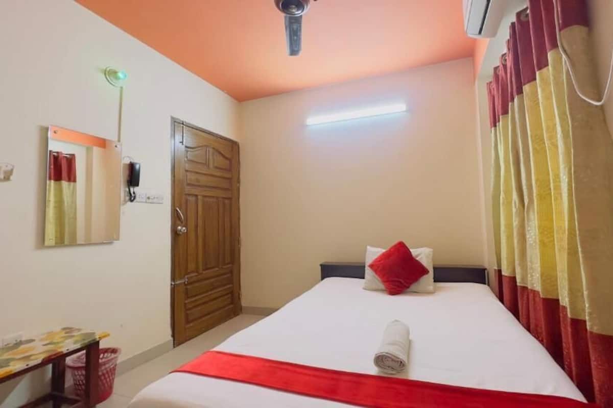 A hotel room with a bed, a desk, a mirror, a door, and a ceiling fan.