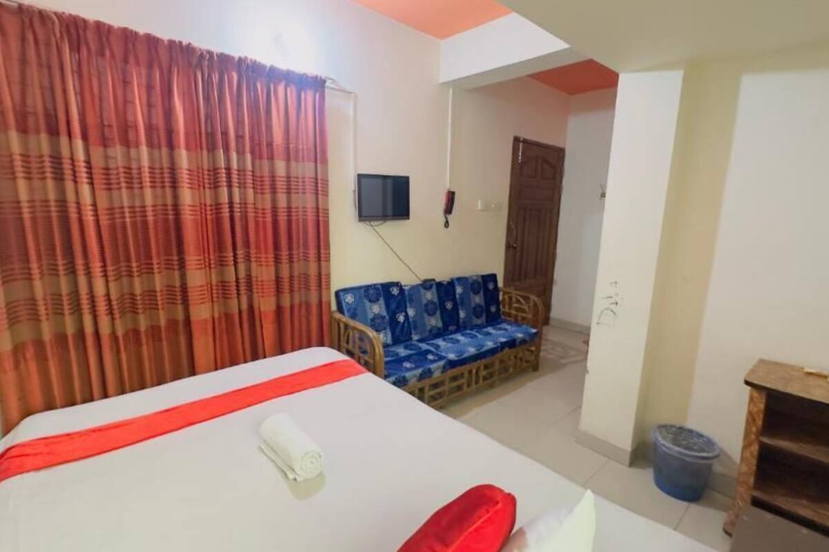 A hotel room with a bed, a sofa, a television, and a wooden cabinet.