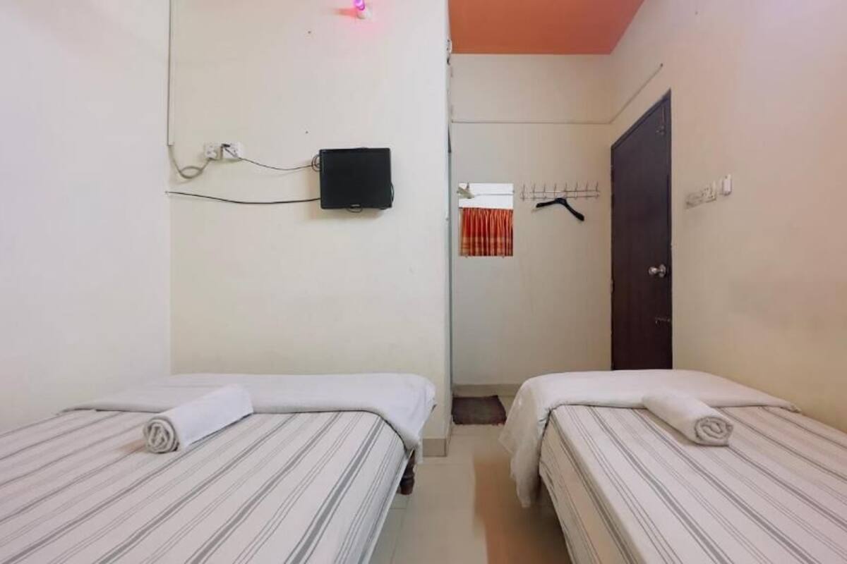 A small, simple room with two single beds, a TV mounted on the wall, and a door leading to another room.