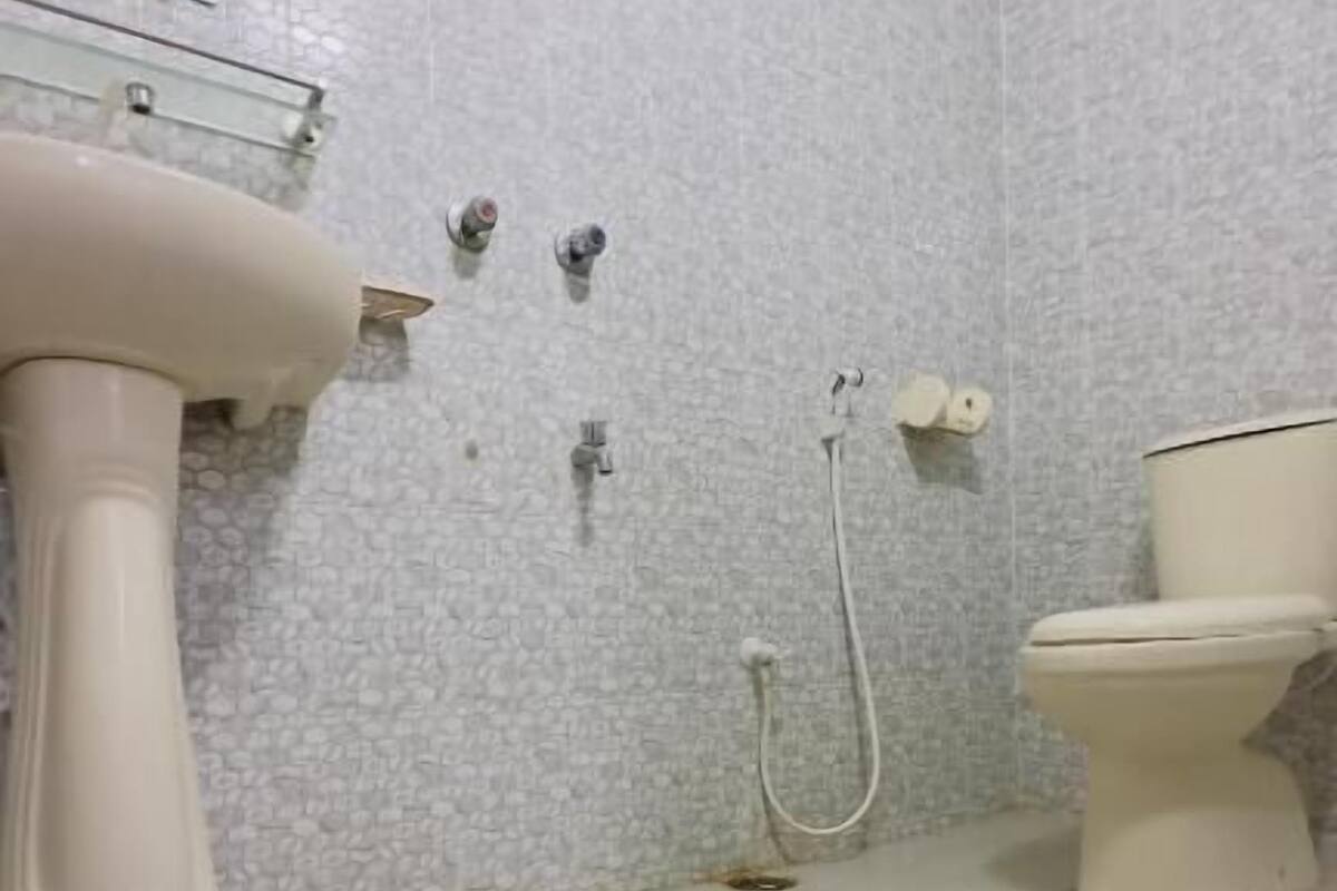 A bathroom with a white tiled floor, a pedestal sink, a toilet, and a shower with a handheld showerhead.