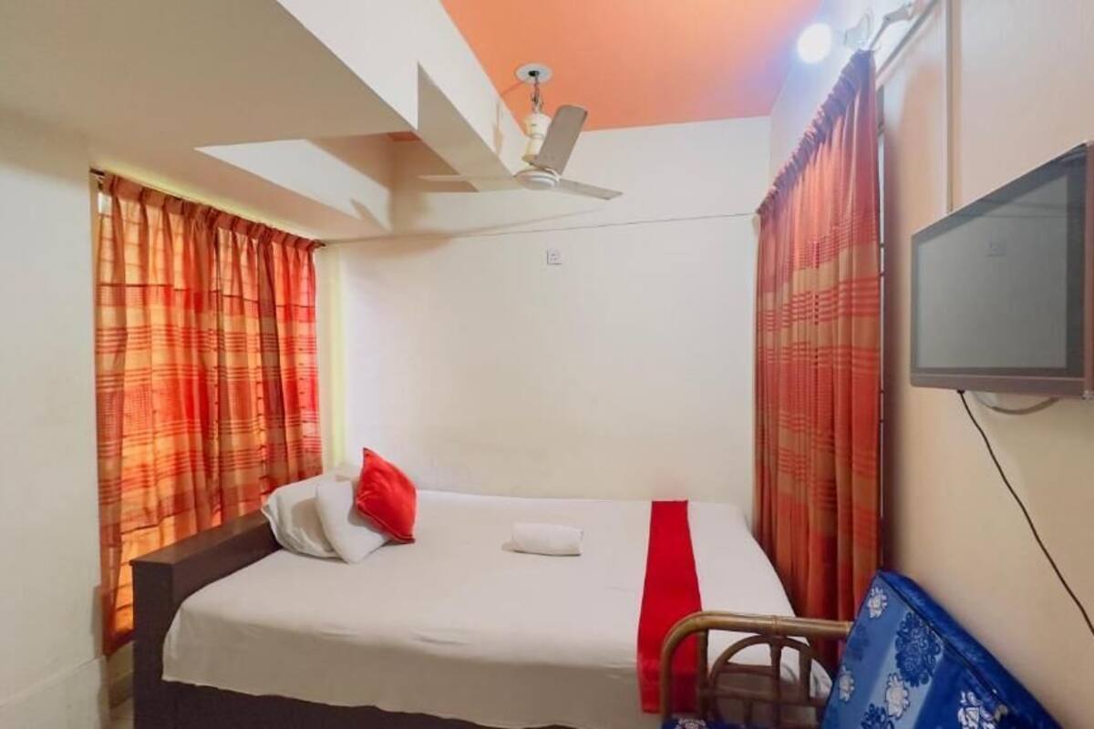 A single bed with a white mattress, red and white striped curtains, a ceiling fan, and a mounted television on the wall.