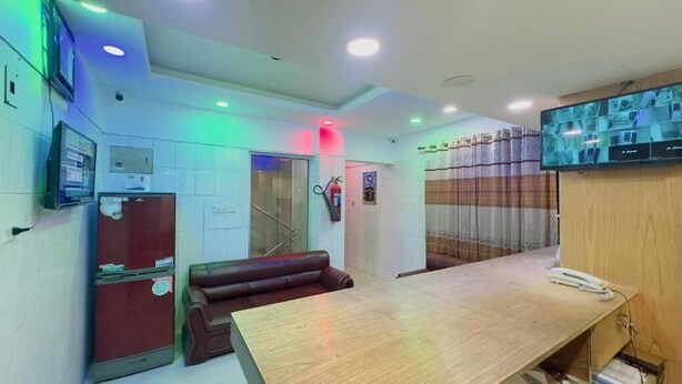 A hotel lobby with a reception desk, a seating area, a fire extinguisher, a television, and a wall-mounted security camera. - Hotel The Sylhet Int. (Dhaka)