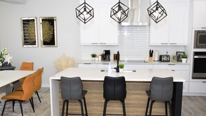 A modern kitchen with white cabinets, a central island with bar stools, and pendant lighting.