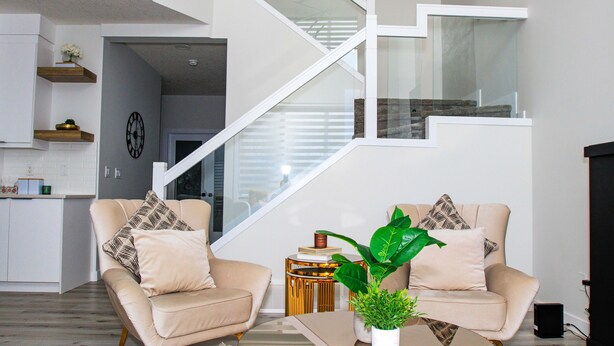 A modern living room with a staircase, beige sofas, and a potted plant.