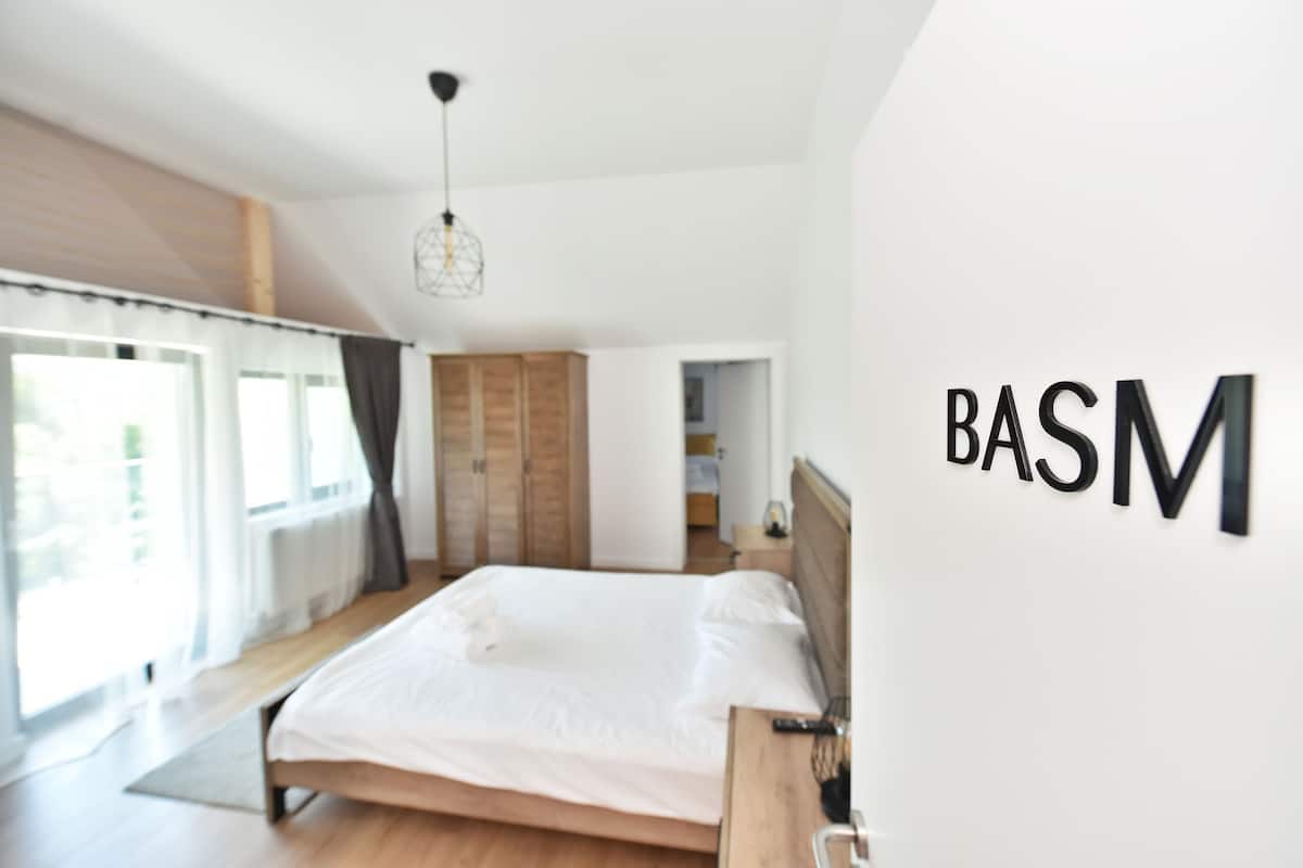 A modern bedroom with a large bed, wooden floor, and a large window.