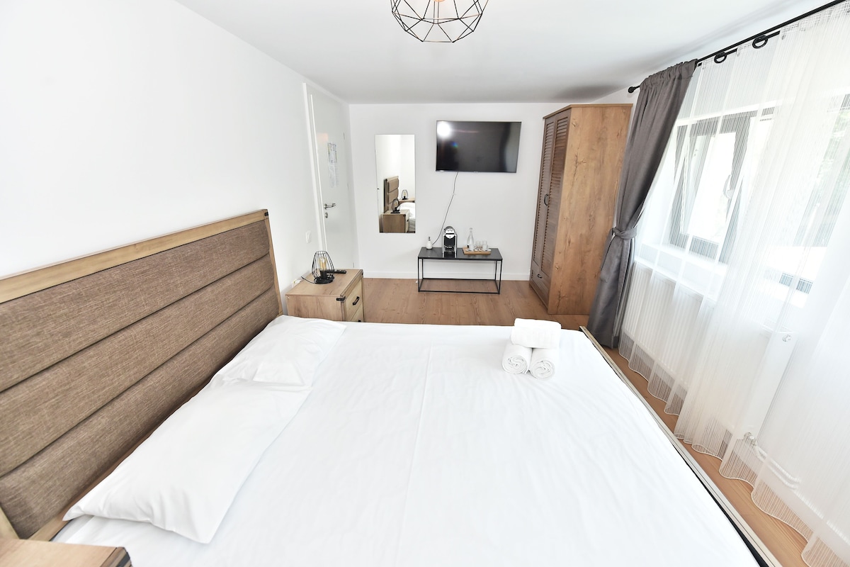 A hotel room with a large bed, a bedside table, a TV, a mirror, and a wardrobe.