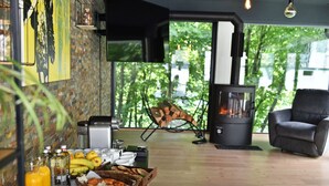 A modern living room with a fireplace, a dining area with breakfast items, and a large window with a view of trees.