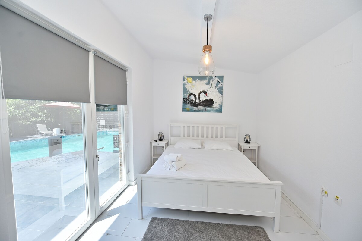 A bedroom with a bed, a nightstand, a painting, and a view of a swimming pool.