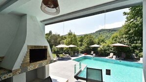 A poolside area with a built-in TV, outdoor seating, and a view of a mountainous landscape.