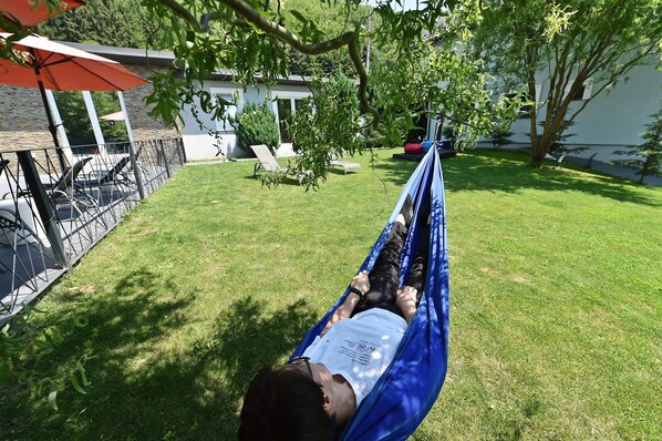 A person lying in a hammock in a grassy backyard with a patio area and a building in the background. - Mira by Atra (Valea Doftanei)