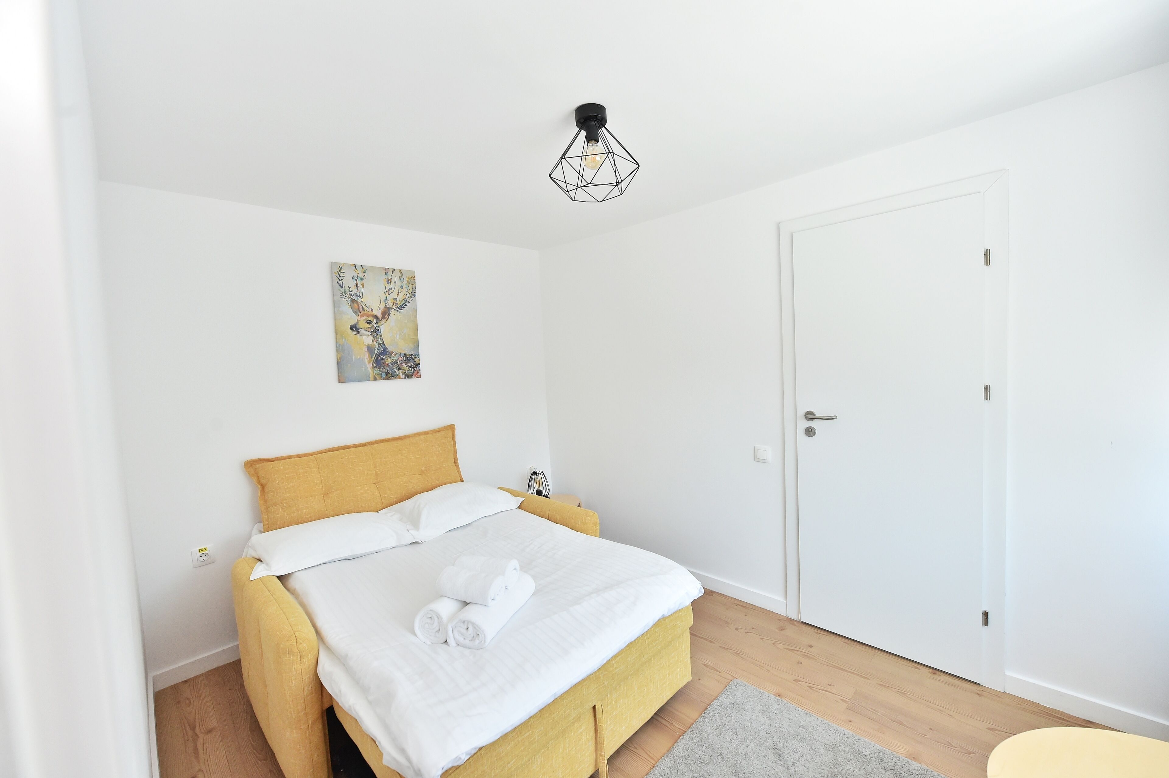 Ein sauberes, modernes Schlafzimmer mit Bett, Nachttisch, Tür und Deckenleuchte.