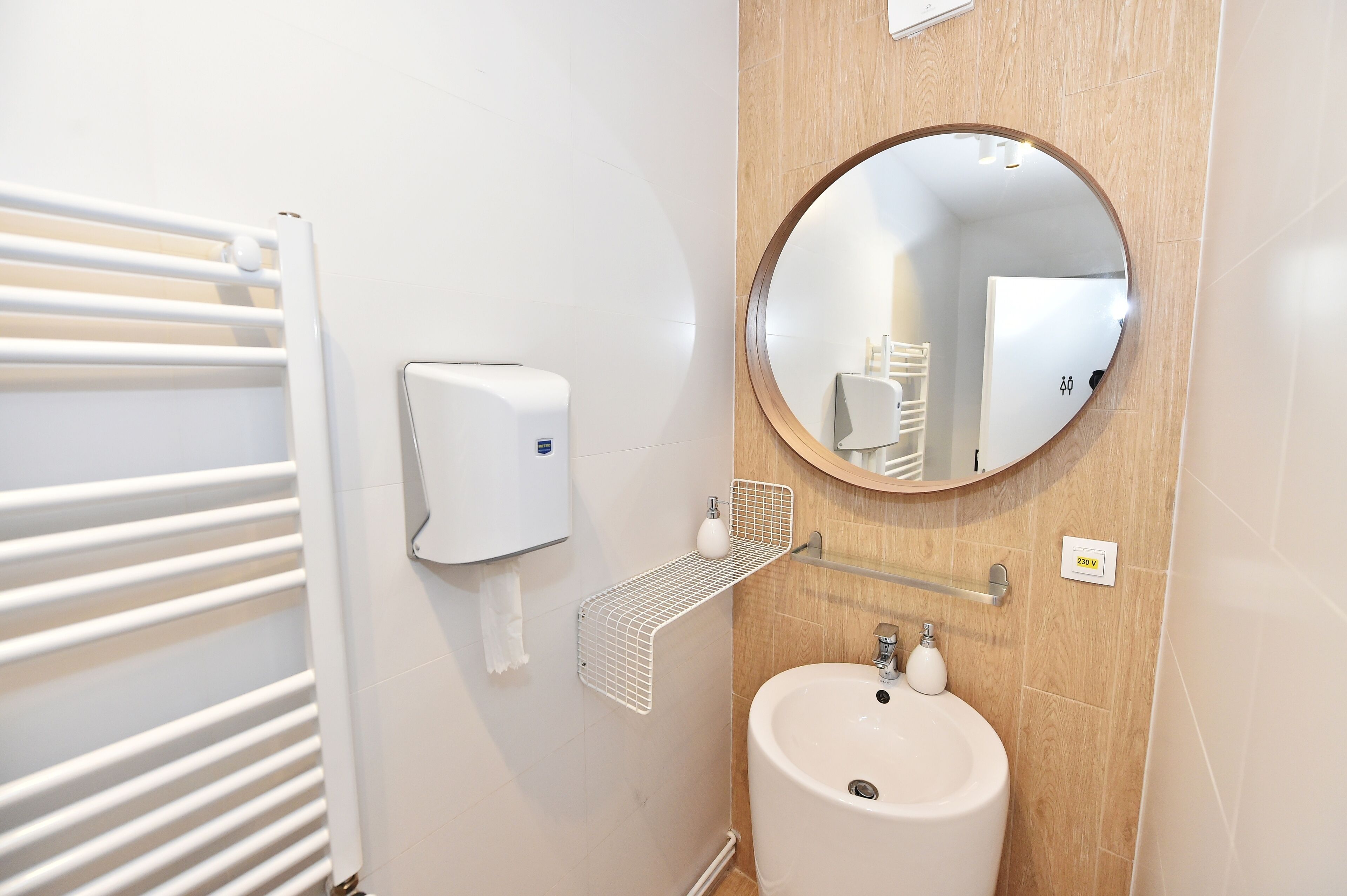 A bathroom with a white radiator, a soap dispenser, a mirror, and a sink.