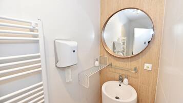 A bathroom with a white radiator, a soap dispenser, a mirror, and a sink.
