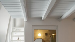 A staircase leading to a bathroom with a round mirror, a sink, and a shower. - Yi & Thalassa by KHI Collection (Kithnos)