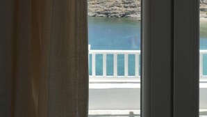 A view from a window with a curtain, overlooking a body of water and a rocky shoreline. - Yi & Thalassa by KHI Collection (Kithnos)