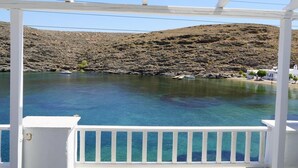 A coastal view from a covered balcony with a clear blue sea and rocky hills in the background. - Yi & Thalassa by KHI Collection (Kithnos)