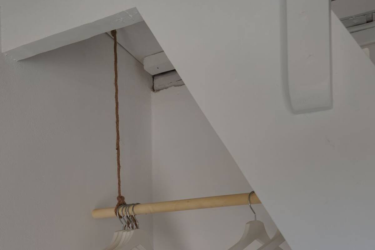 Un coin de pièce avec un banc en bois, un mur blanc et une poutre en bois sur laquelle est fixée une corde et deux cintres blancs.