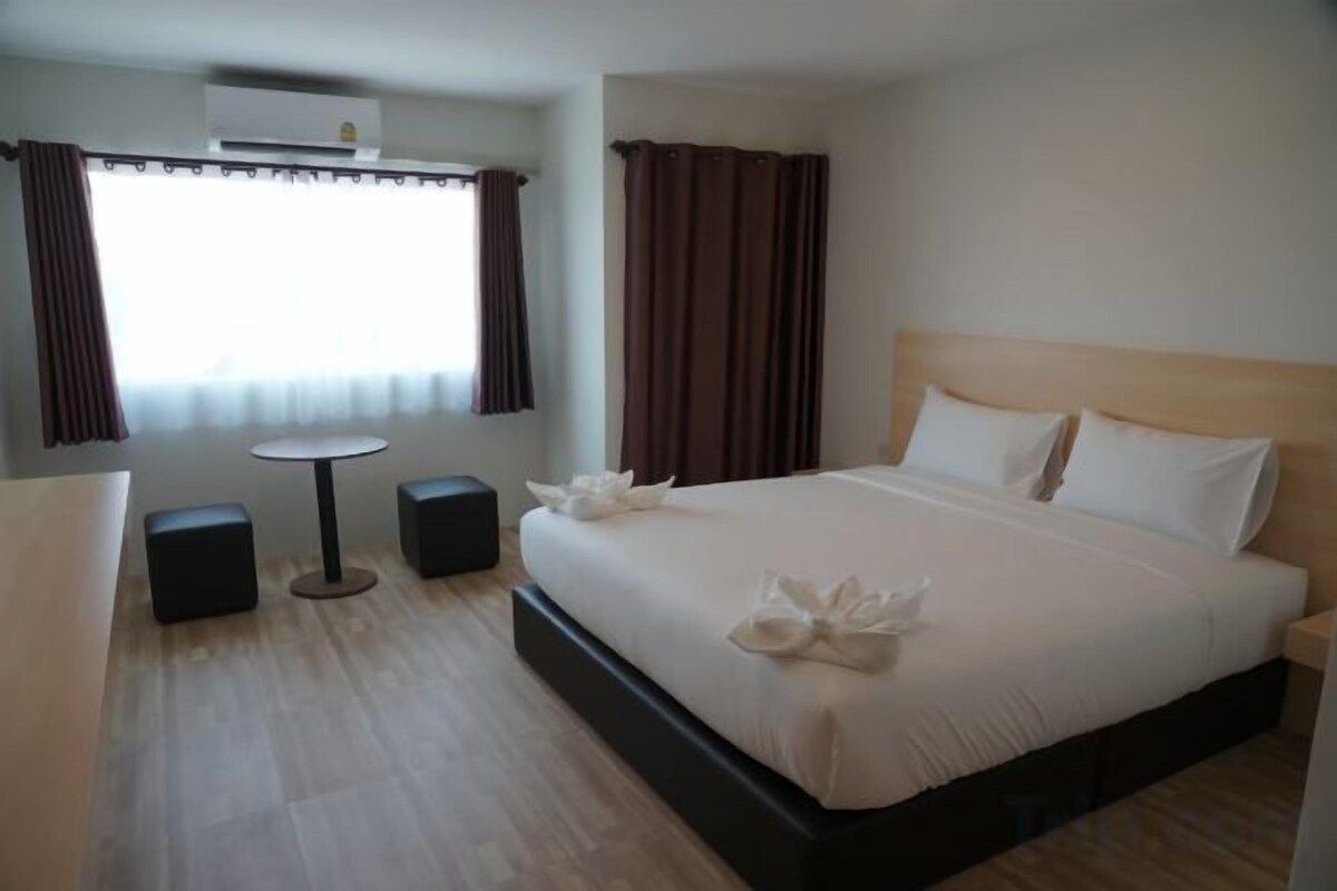 A hotel room with a bed, a round table, two chairs, a small table, and a window with curtains.