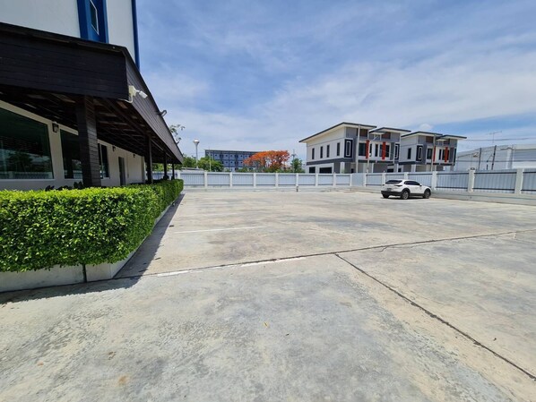 A parking lot with a white car, a building with a modern design, and a clear sky. - The Charlotte Smart Hotel Lopburi (Lop Buri)