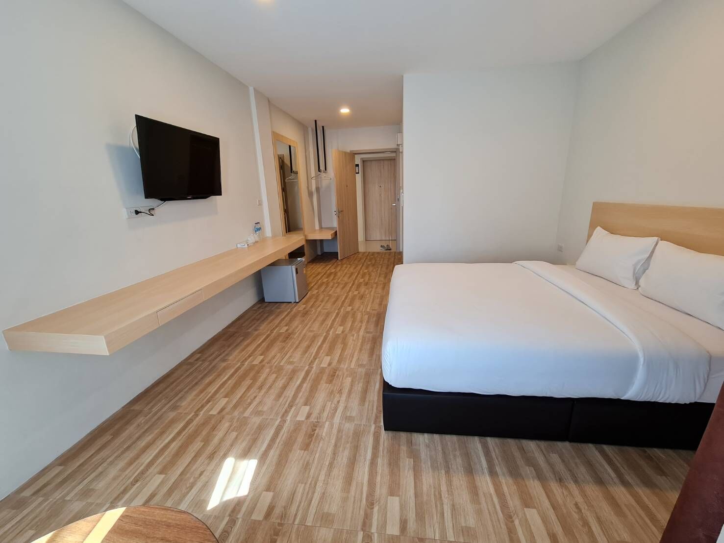 A hotel room with a bed, a TV mounted on the wall, a wooden floor, and a small desk with a chair.