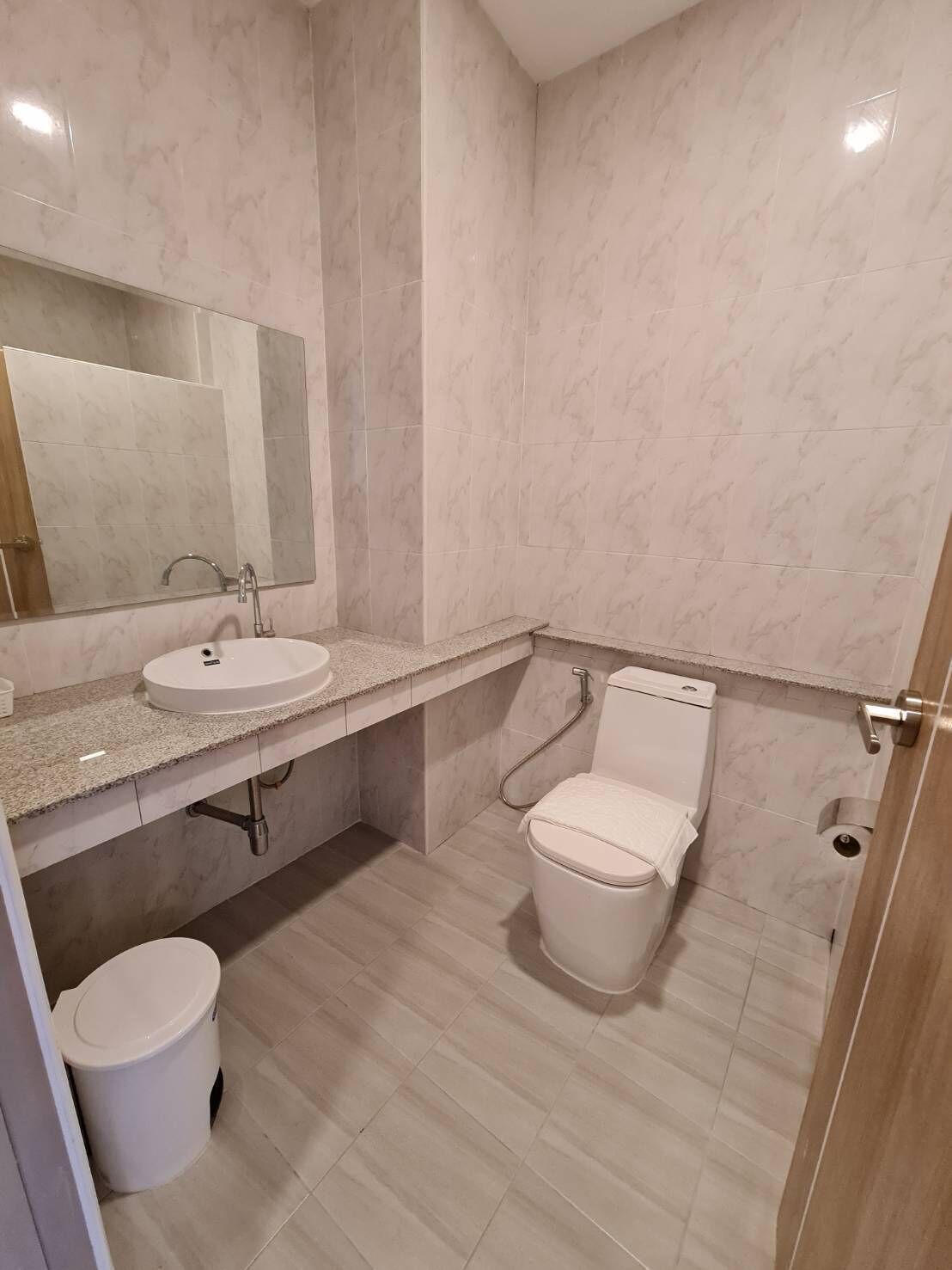A bathroom with a sink, mirror, toilet, and a trash bin.